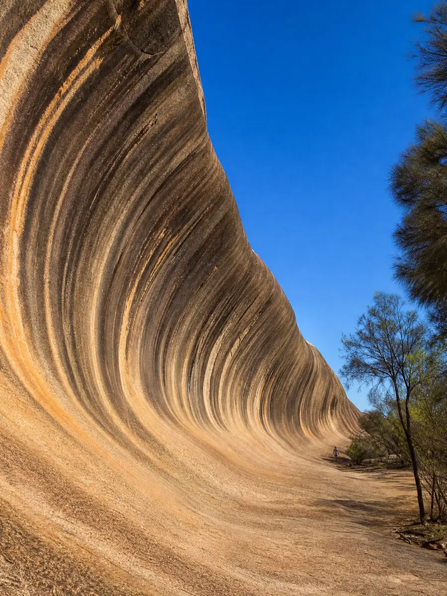 Looking up into the curl of Wave Rock, its striped granite overhanging against a blue sky